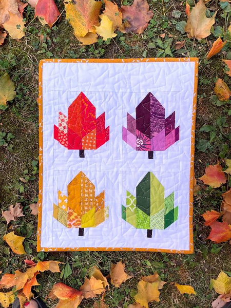 a quilt featuring 4 paper pieced leaves in red, orange, purple, green