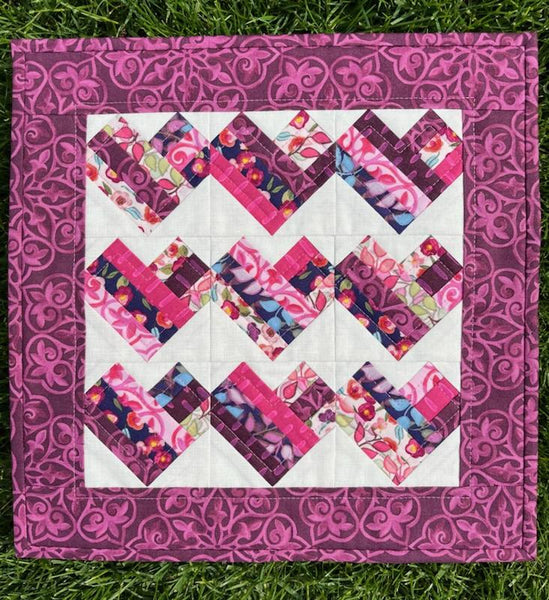 Foundation Paper Pieced mini quilt featuring panels of hearts made with fabric scraps in pink, red, and purple set against a white backdrop