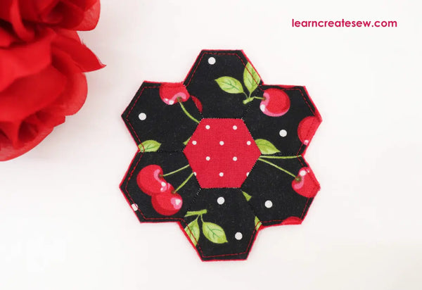 A paper pieced coaster composed of 7 hexagon fabric pieces arranged in a floral design