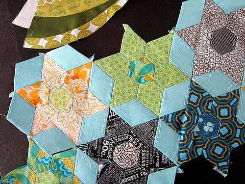 An English Paper Pieced pattern in progress features multicolored triangles set in a 6-sided star design