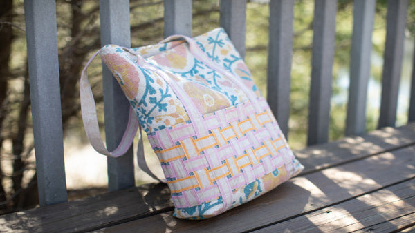 Quilted tote lying on park bench composed of fabric strips in a woven design