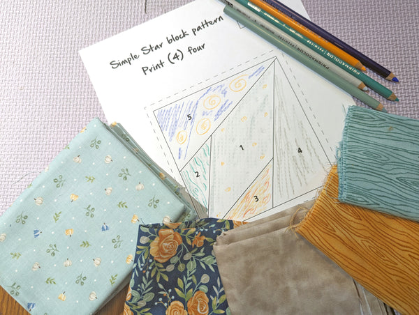 selection of fabrics laid on top of paper with foundation paper piecing pattern colored in with color pencils