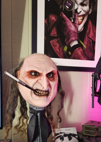 Photo of the PureArts Batman Returns The Penguin Art Mask in front of a framed poster of The Joker