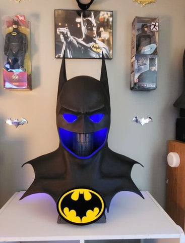 PureArts Batman 1989 Cowl affiché avec une lumière bleue à l'intérieur devant d'autres objets de collection Batman.