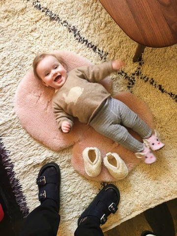 Baby lying onto of Binibamba sheepskin snuggles, a natural, hypoallergenic playmat in Rose pink that  also doubles up as a buggy liner in rose pink.