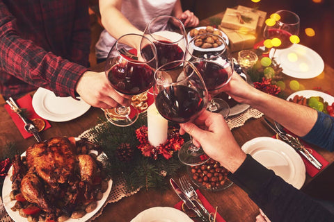 Christmas table with turkey and festive food and people cheering with red wine in glasses