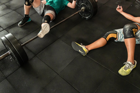 TWO PEOPLE LAYING ON THE GYM FLOOR WITH A BARBELL