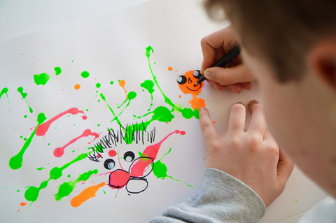Kind zeichnet Gesichter in Farbklecks