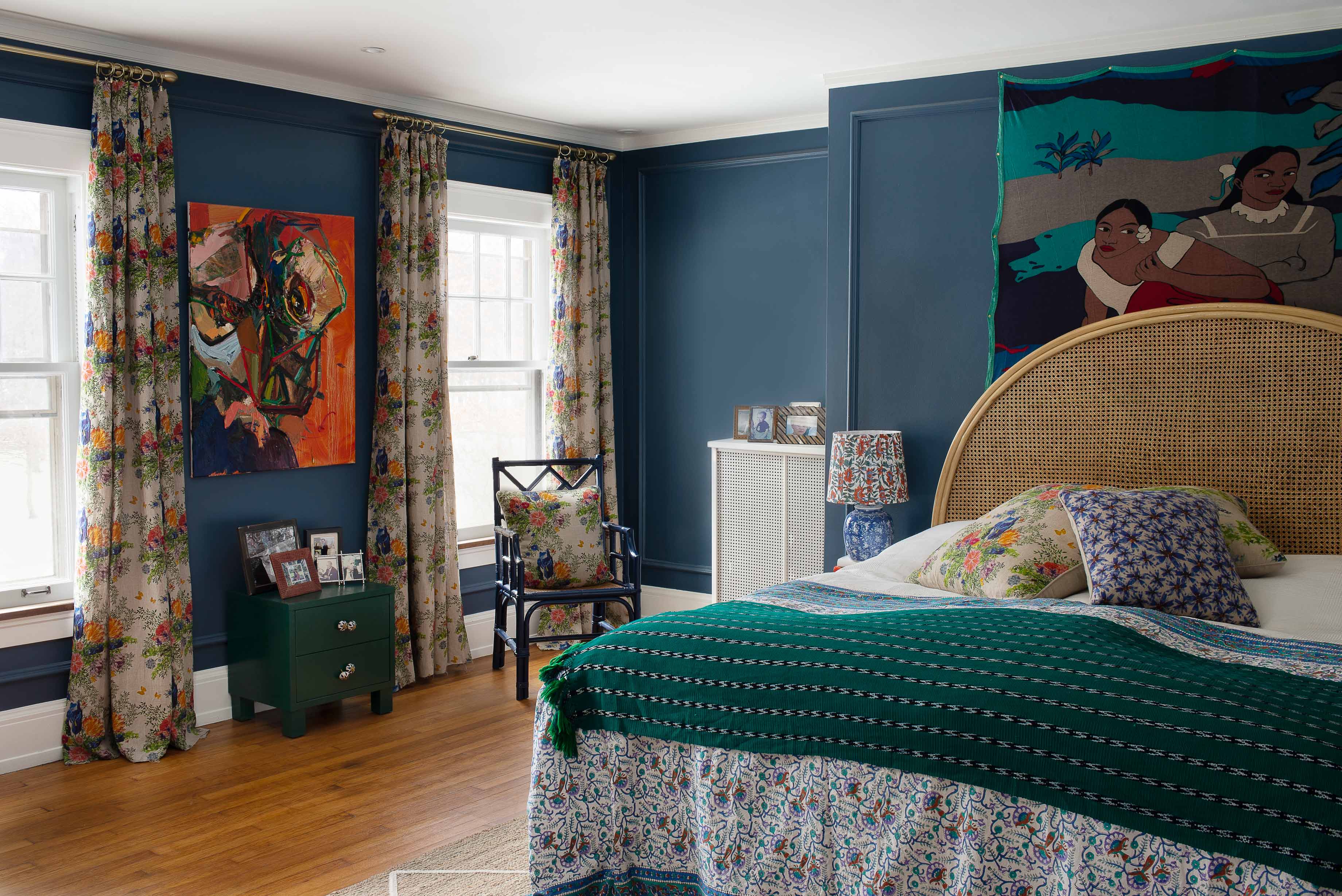 Blue painted bedroom with floral print linen curtains, colorful art and organic linen throwpillows on the bed.