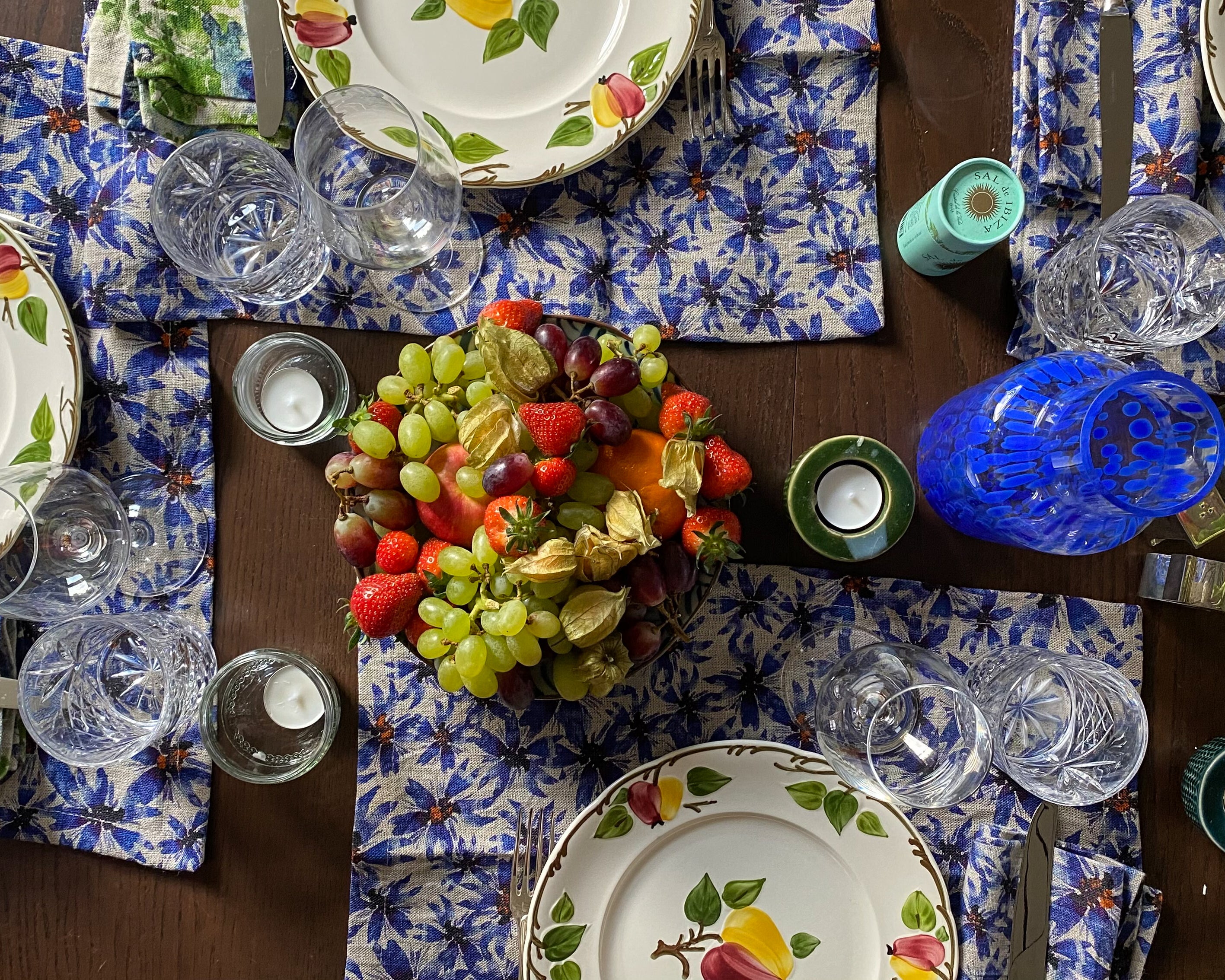 Gedeckter Tisch mit blauer Blumentischwäsche und Obstteller-Dekor.