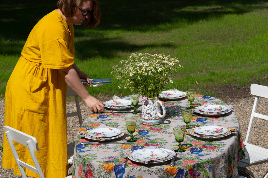 Sophie is setting the table with an organic linen tablecloth printed in floral patterns and colorful plates and glasses