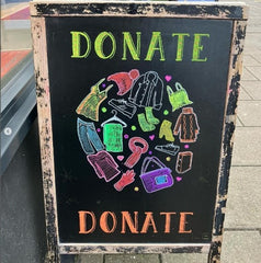 A blackboard sign with a chalk drawing of clothing made yup in a globe shape. Text reads 'Donate'.