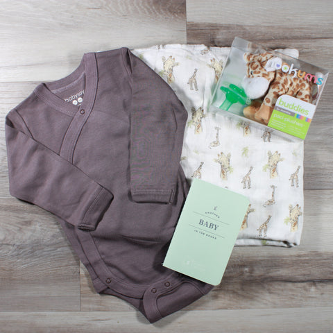 Contents of the Bundle of Joy - Giraffe baby gift box available at Doromania. Flat lay of baby onesie, swaddle, pacifier plushie, and baby journal.