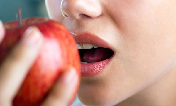 What helps against gingivitis? – Woman biting into apple (healthy diet)