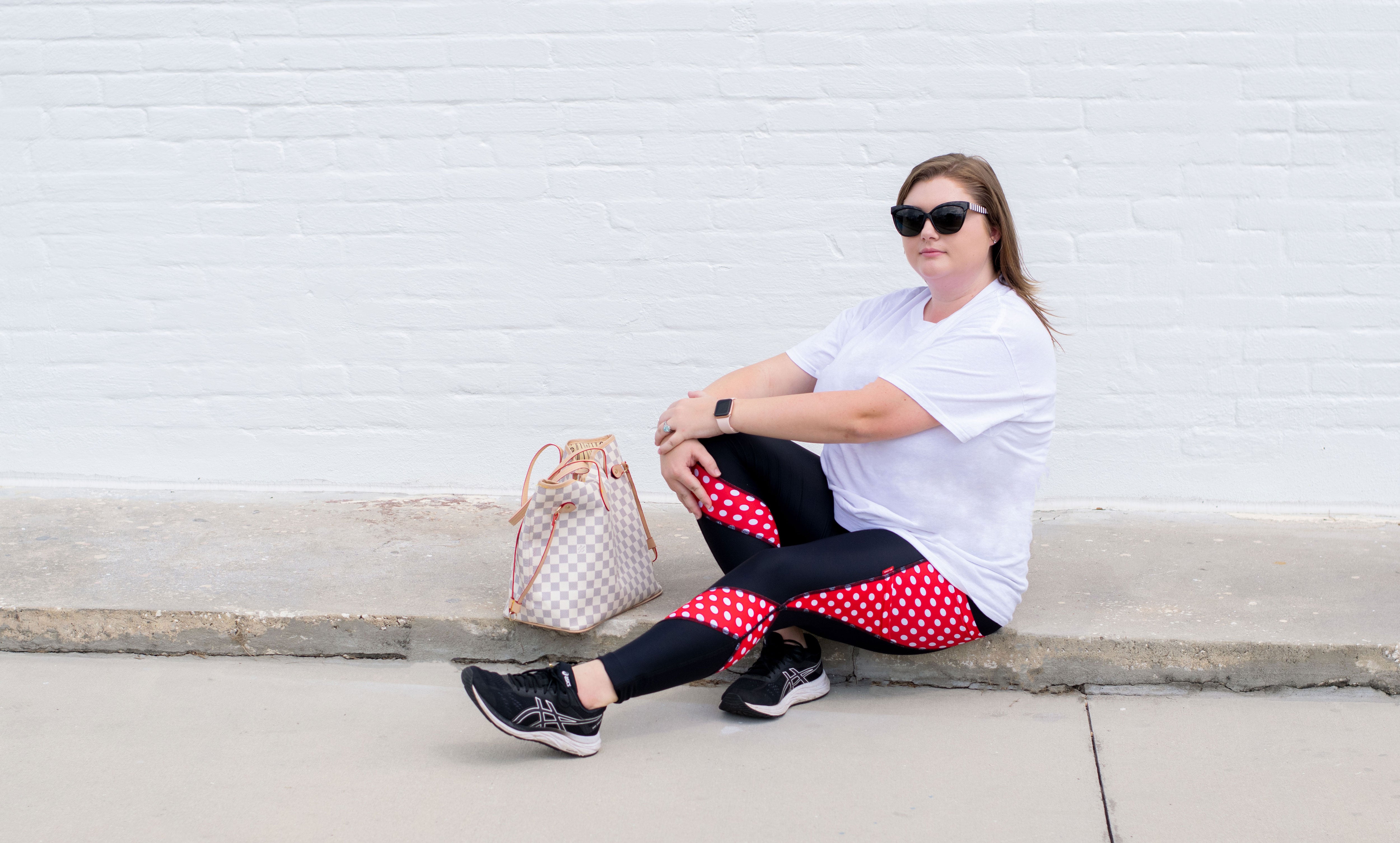 Model sitting on sidewalk in front of color wall wearing Red Mini Tech leggings