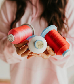 Spools of pink, red and white embroidery thread in the founder's hands