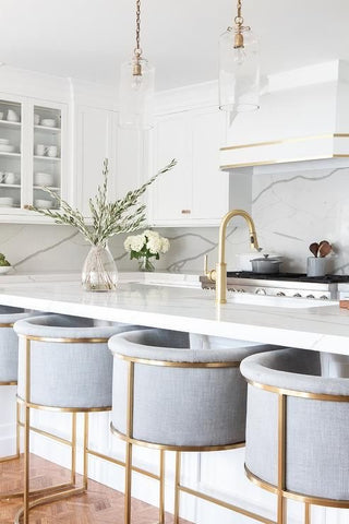 An array of velvet kitchen chairs with brass frames against a marble kitchen island