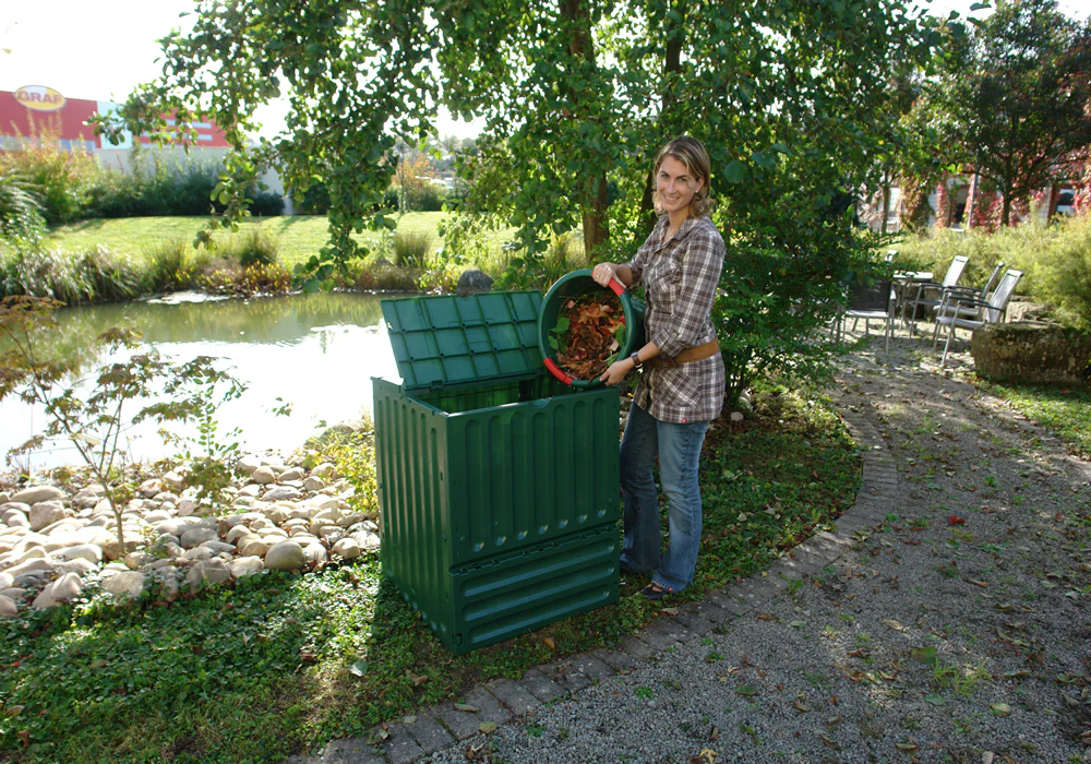 Woman composting leaves in green compost bin in garden setting