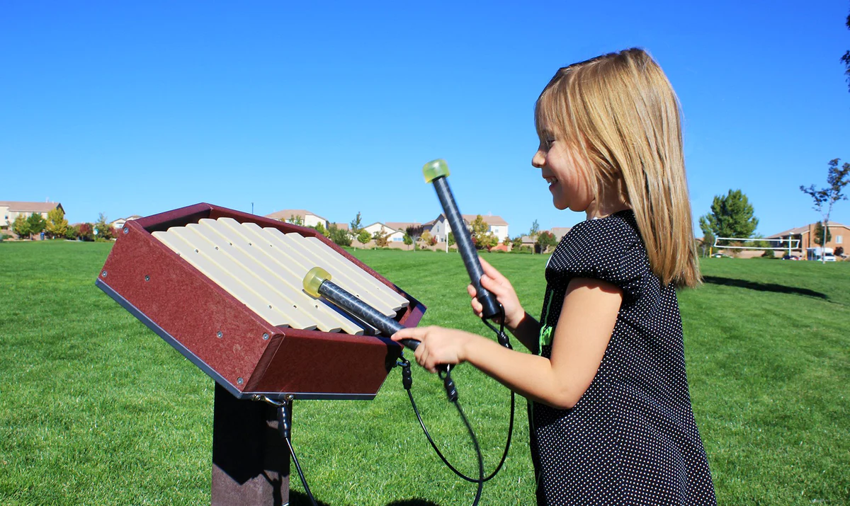Young girl playing outdoor xylophone instrument in park