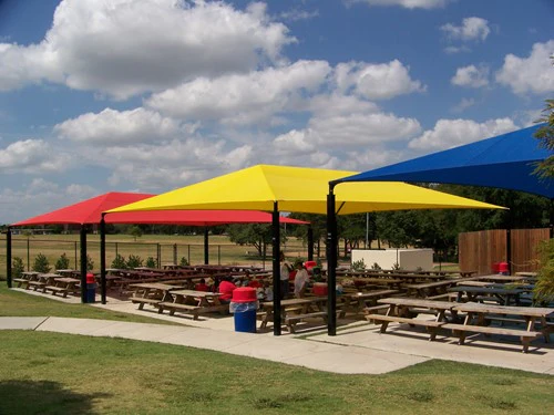 Colorful outdoor park picnic area with red, yellow, and blue canopies over wooden tables
