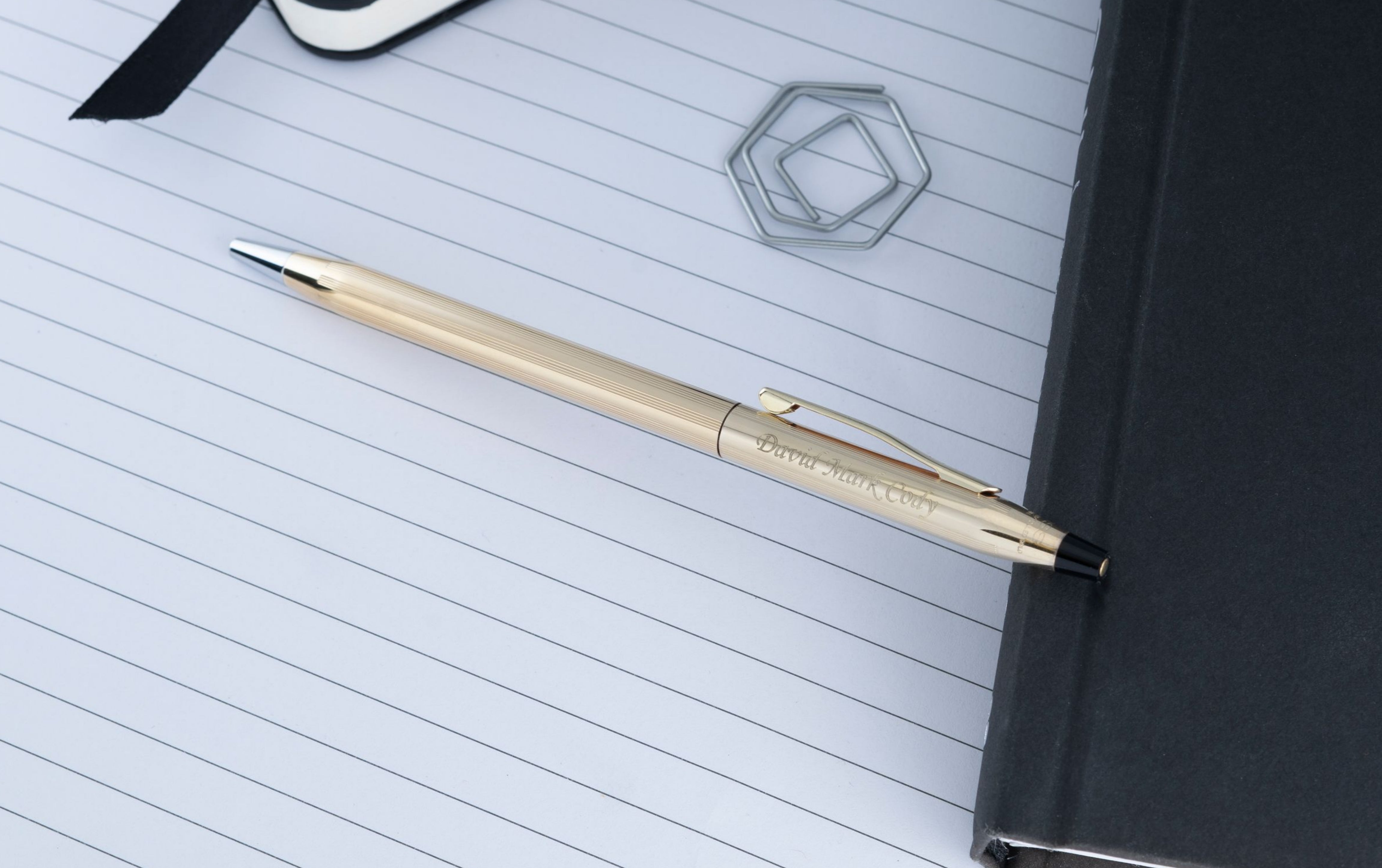 Engraved Classic Century Gold Ballpoint placed on notebook with desk items