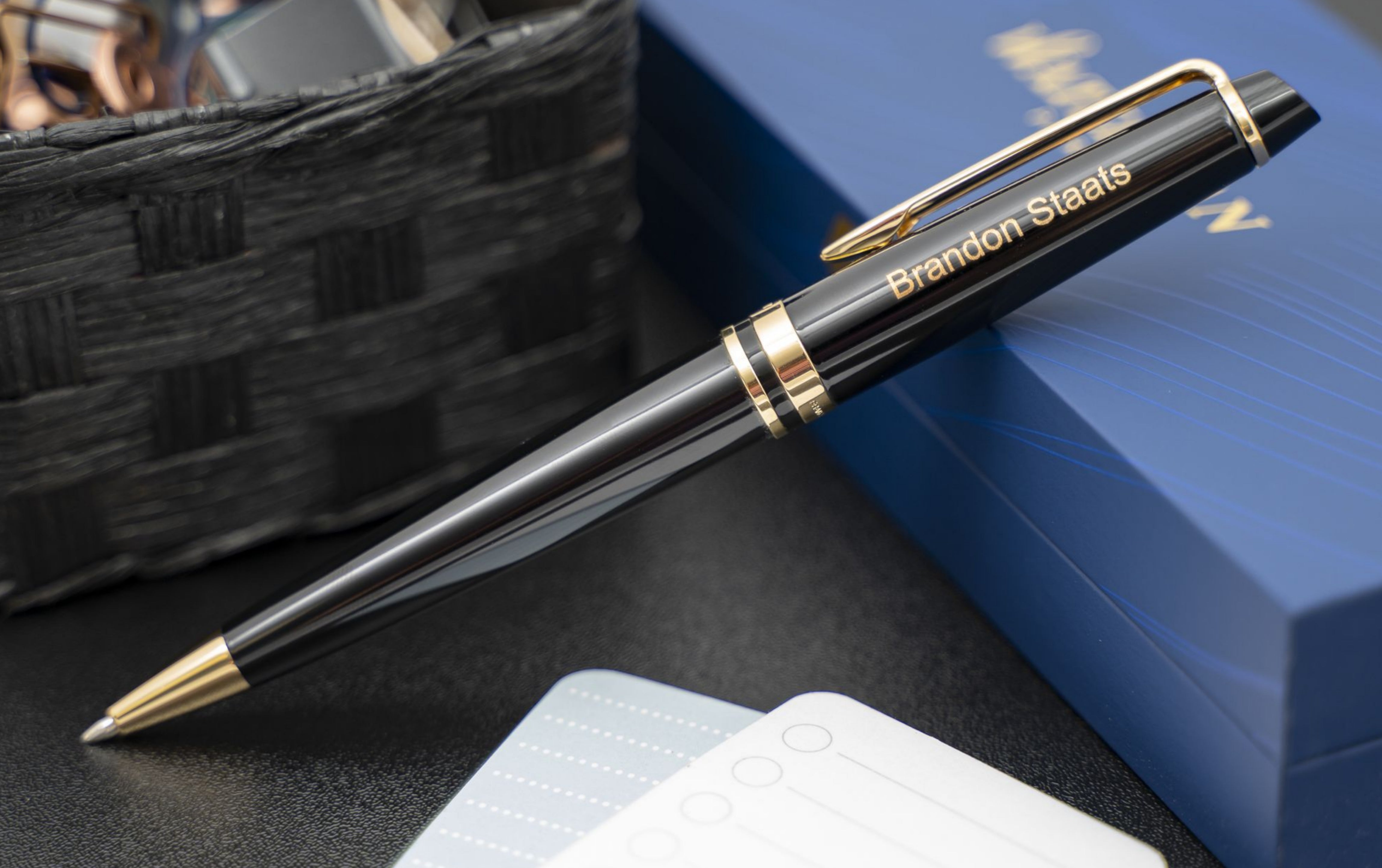 Engraved Expert Black Ballpoint placed on blue box with desk items