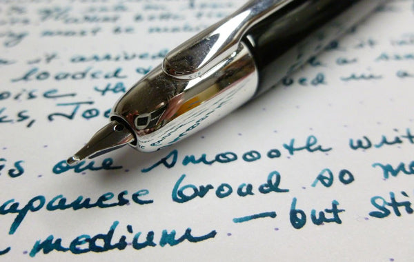 Pen with a broad silver-colored nib lying on a white paper surface with many sentences written in bold