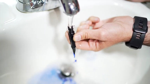 A man flushing out blue ink from his black fountain pen nib under a tap of running water