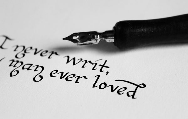 Narrow barrel fountain pen lying on a brilliant white paper pad with the poetry lines: ‘I never writ, man ever loved’ written in deep black ink