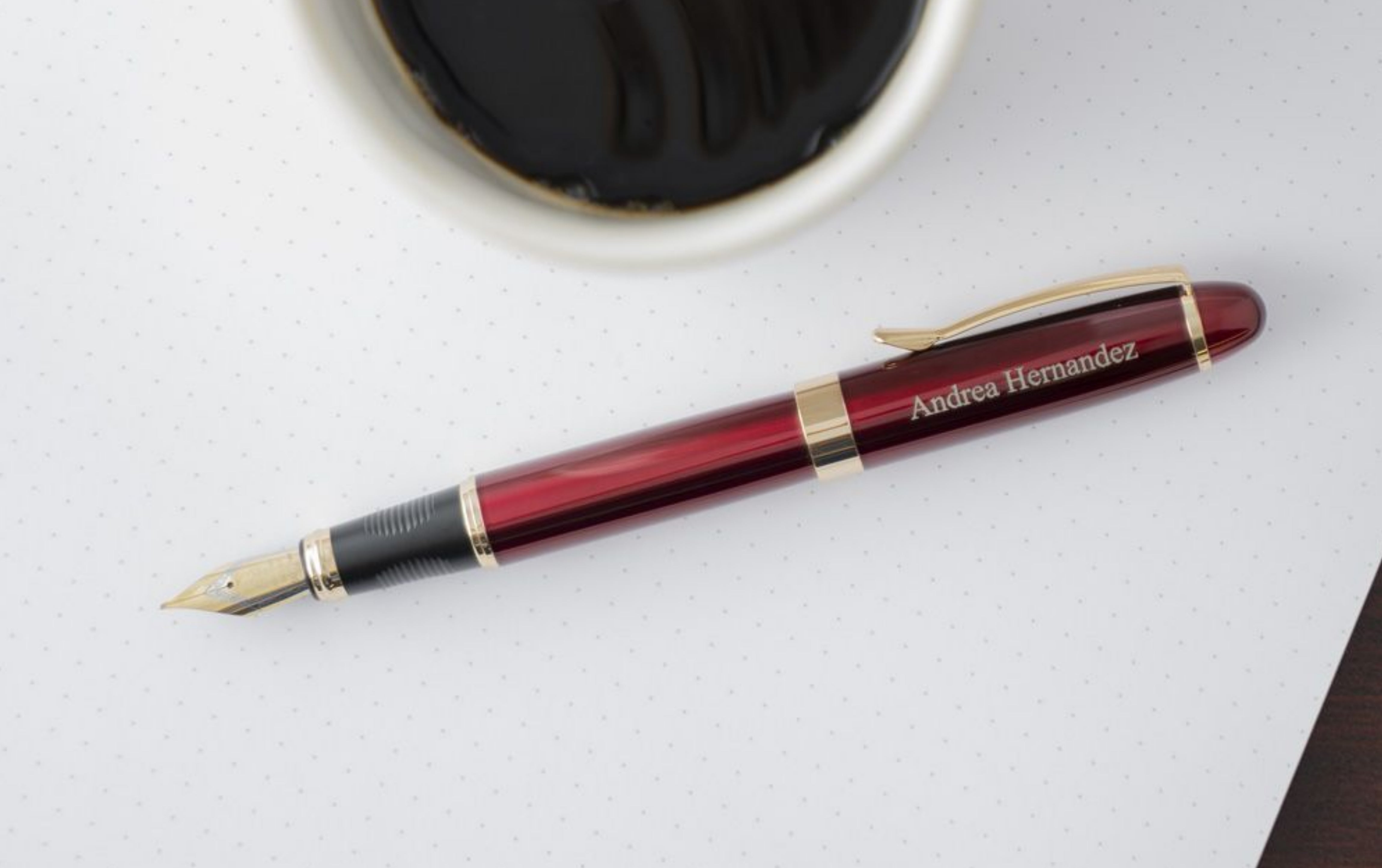 Engraved Red Alexandria Fountain Pen next to a cup of coffee