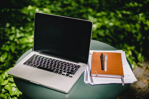 Laptop and diary on table in garden with pens