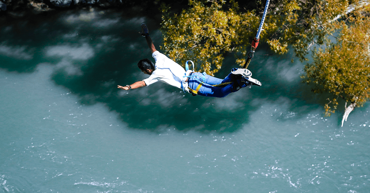 A man bungee jumping over a light blue river