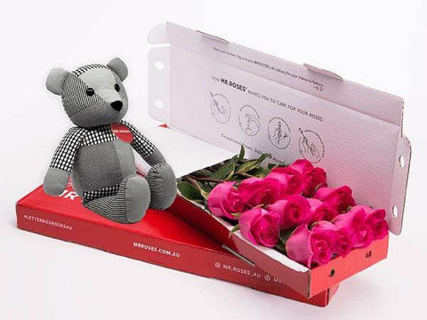 cute grey teddy bear sitting next to a box of medium stemmed bright pink roses from mr roses