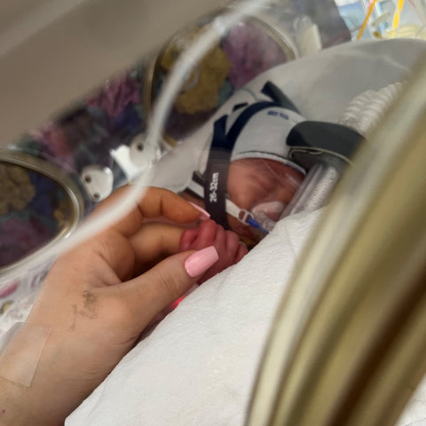 Mum's hand holding onto Premature Baby in isolette 