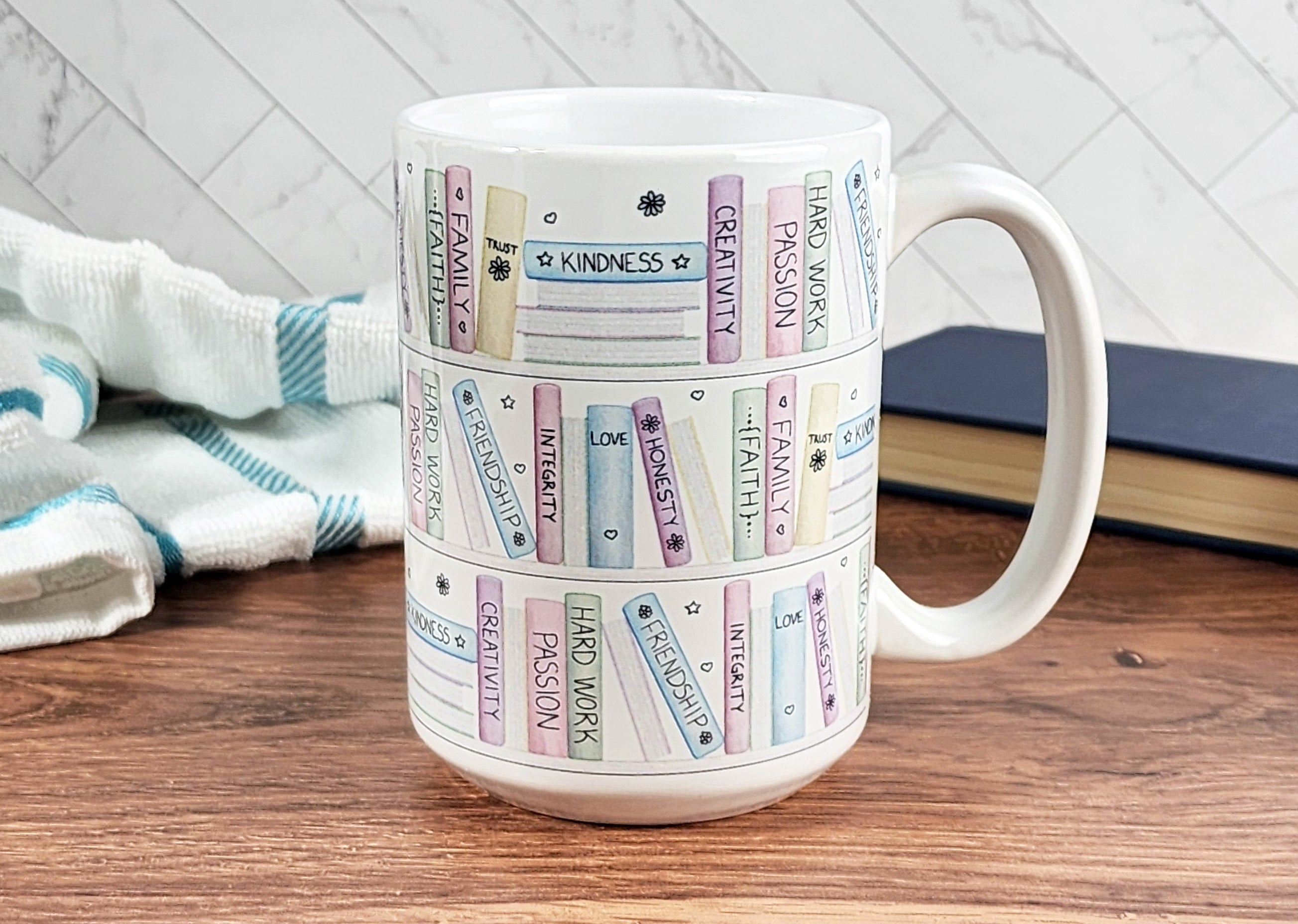 The Building Books of Life - Inspirational Mug in the 15oz size on a tabletop next to a tea towel and a book.