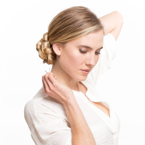Blonde haired model using bobby pins to secure her updo hairstyle wearing a white shirt using Easy Updo Extensions