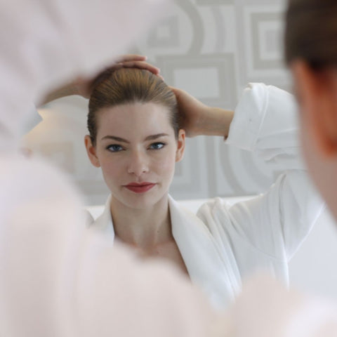Pretty woman getting ready in the morning putting her hair up in a bun wearing a white robe and red lipstick