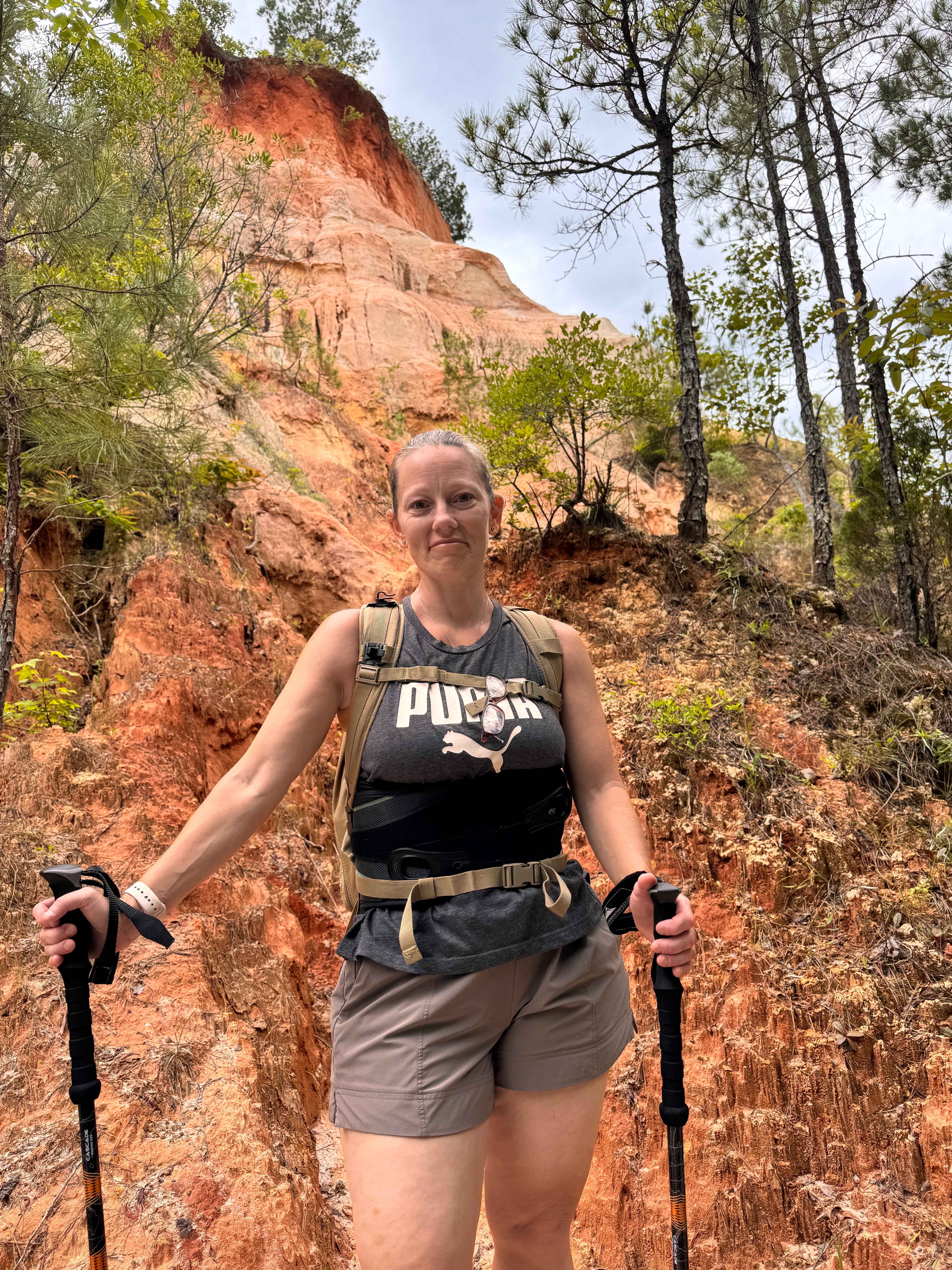 Me, Shawna, posing with hiking backpack and trekking poles in a canyon at Providence Canyon State Park, Georgia. The rim of the canyon is more than 100 feet above my head.