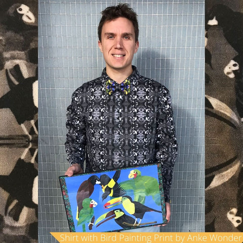 Model wears a black and white shirt with bird print and holds a painting of birds in his hands.