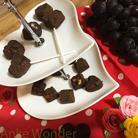 Chocolate pralines on a white two tiered server in heart shape with flowers and grapes around it.