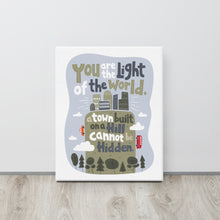 Load image into Gallery viewer, A canvas is leaning against a wall on the floor. The artwork is on a white background with lettering reading &quot;You are the light of the world, a town built on a hill cannot be hidden.&quot; The words are a light gray background with an illustrated city.