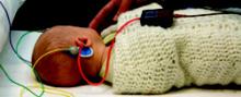 Photo of a baby lying down, wearing earphones and sensors on its head.