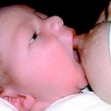 Photo of a baby being brought to the breast, with its mouth wide open and its tongue down, its chin touching the breast.