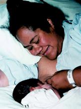 Photo of a woman lying on her side, with her baby facing towards her to feed.