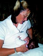 Photo of a woman sitting up, with her baby supported by her right arm, feeding from her left breast.