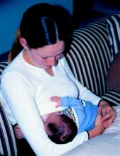 Photo of a woman sitting up, holding her baby against her to feed.