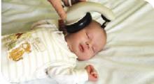 Photo showing baby having the newborn hearing screening with the ear cushion placed over their head. Baby is asleep.