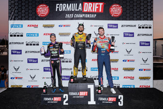 Chelsea DeNofa stands atop the Formula Drift podium in first place with James Deane next to him after finishing in third place