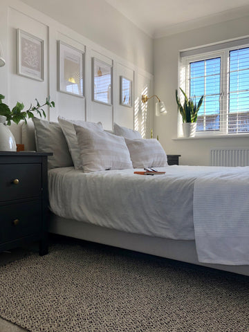 Neutral bedroom aesthetic with white panelling, neutral bedding and four framed artworks hung above the bed