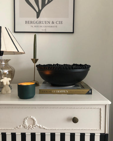 Cream and black striped chest of drawers with a lamp, candles, a Kelly Hoppen book and black upcycled bowl sat on top